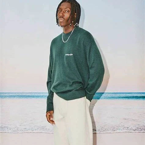 Man wearing oversized hoodie and wide-leg pants, showcasing latest streetwear trends in urban fashion against a beach backdrop.