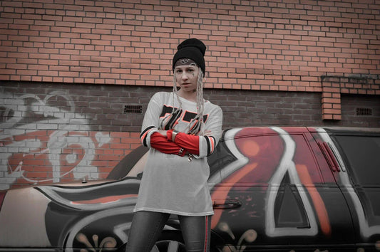 Woman in streetwear fashion style posing in front of a graffiti-covered car, wearing a beanie and oversized shirt, showcasing urban fashion and streetwear aesthetic.