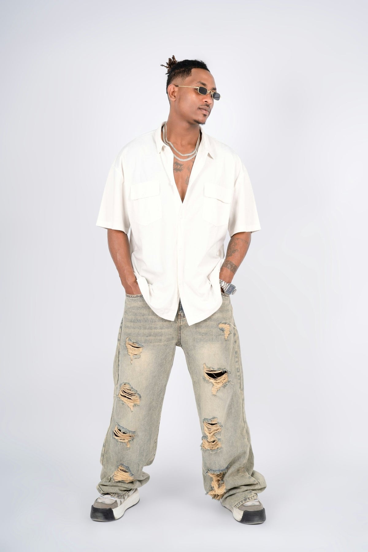 Man wearing baggy ripped denim jeans styled with a relaxed short-sleeve shirt and streetwear sneakers, showcasing an urban streetwear look.