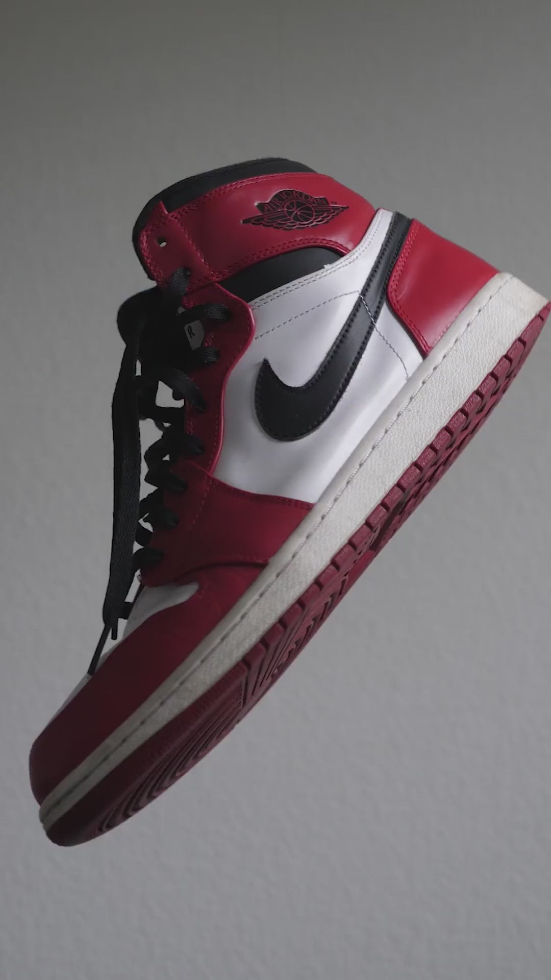 Red, white, and black high-top urban sneakers with a black swoosh logo, red outsole, and black laces, suspended mid-air against a neutral gray background – perfect for urban style.